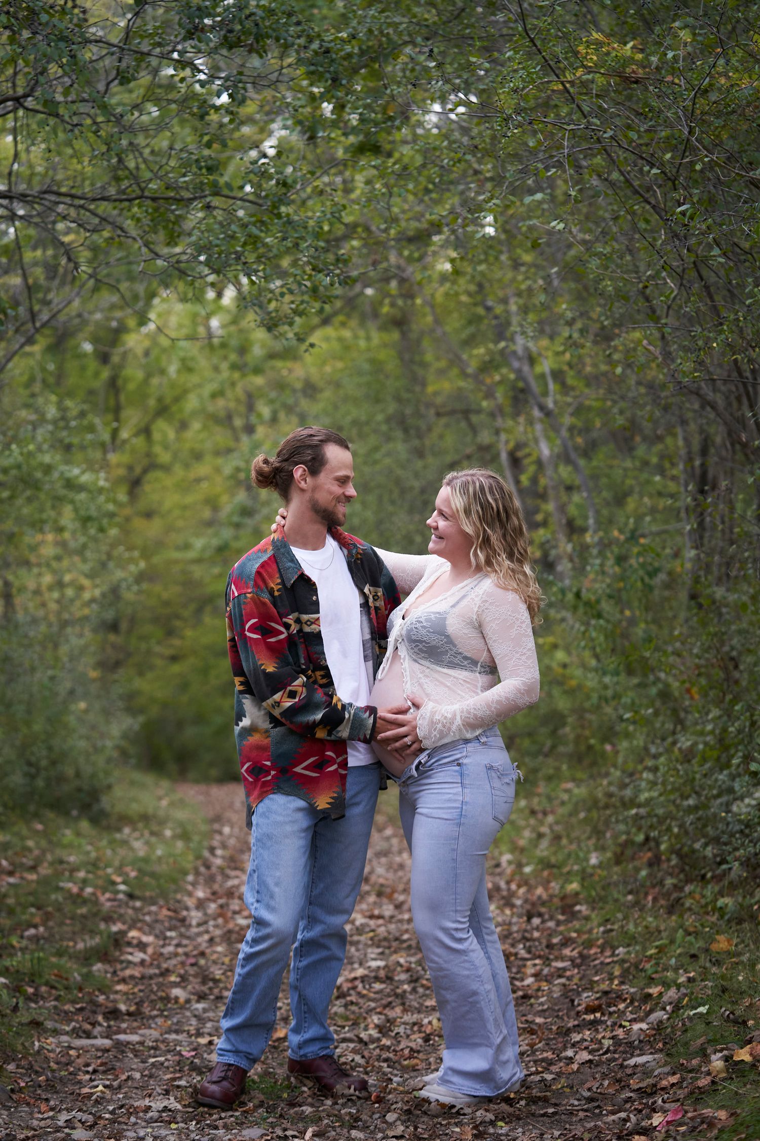 A couple shares a tender moment while walking along a wooded trail on an autumn day.