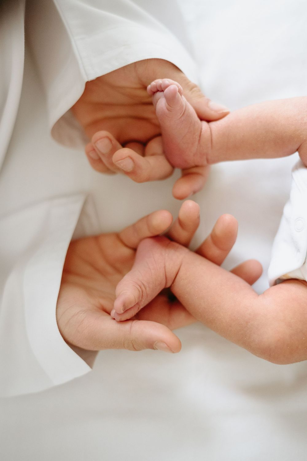 Close-up of a newborn baby's tiny hands and feet resting gently in an adult's caring hands.