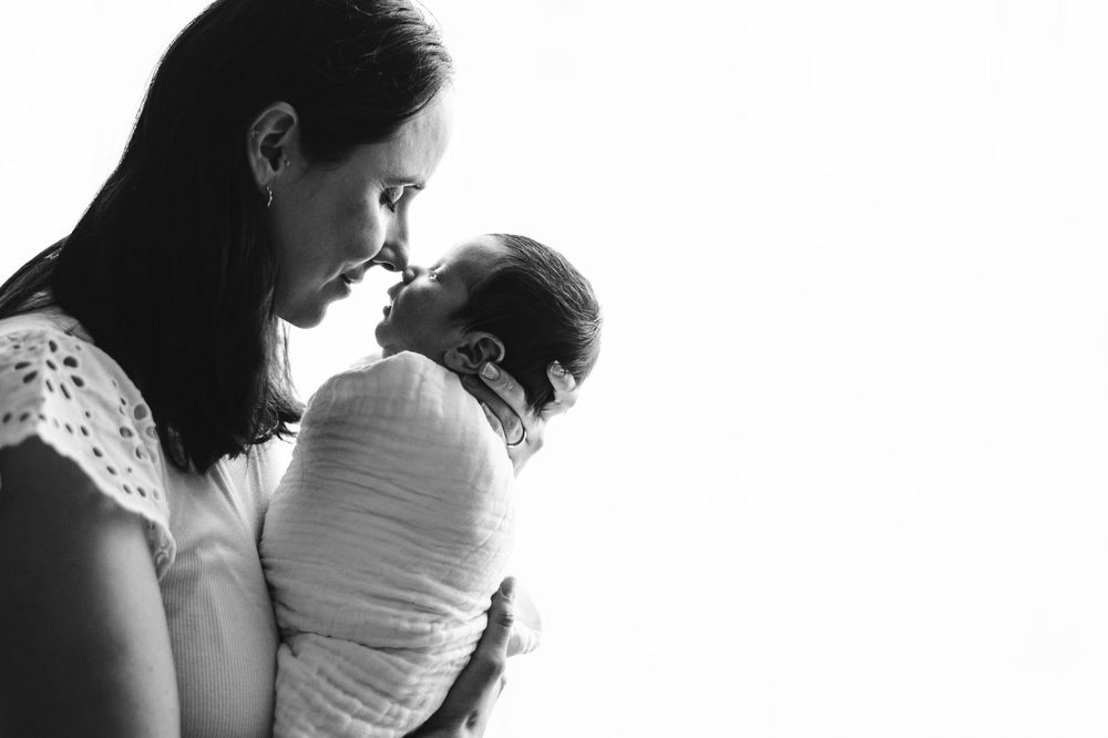Black and white photo of a mother tenderly holding her swaddled newborn baby close to her face.
