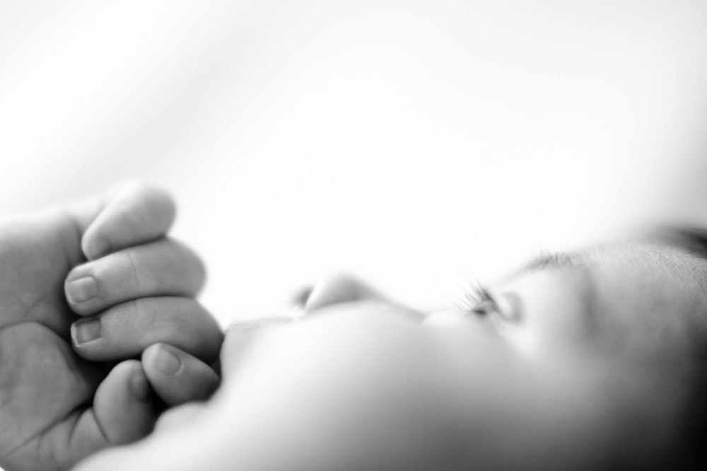 Black and white photo of a newborn baby sleeping while gently gripping an adult's finger.