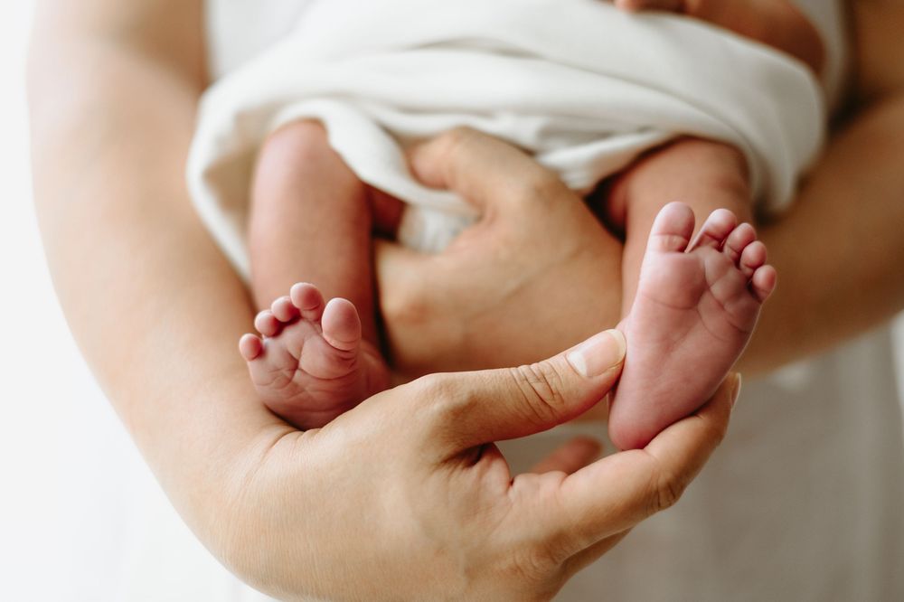 Close-up of a newborn baby's tiny feet held gently in an adult's hands, wrapped in a white blanket.