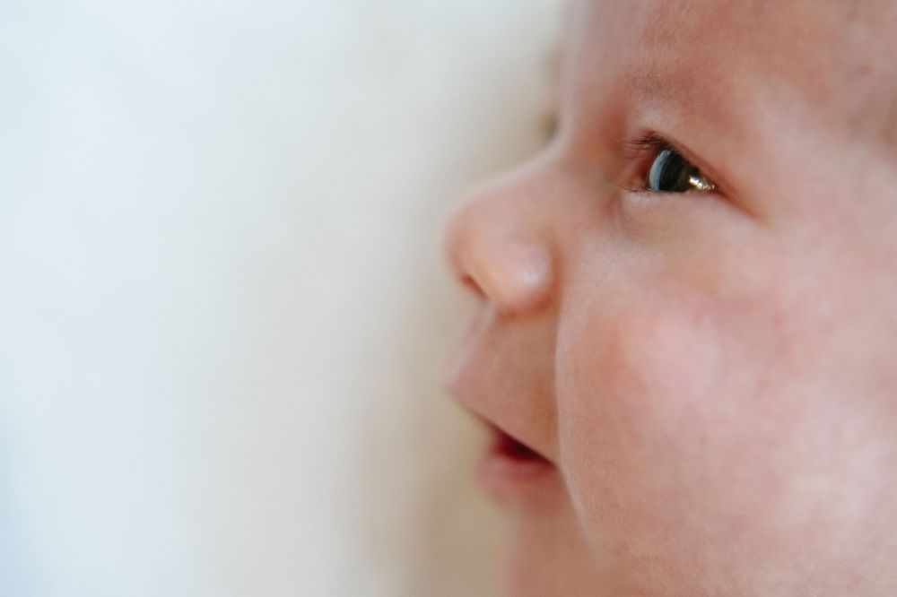 Close-up portrait of a peaceful newborn baby with soft skin looking sideways against a white background.
