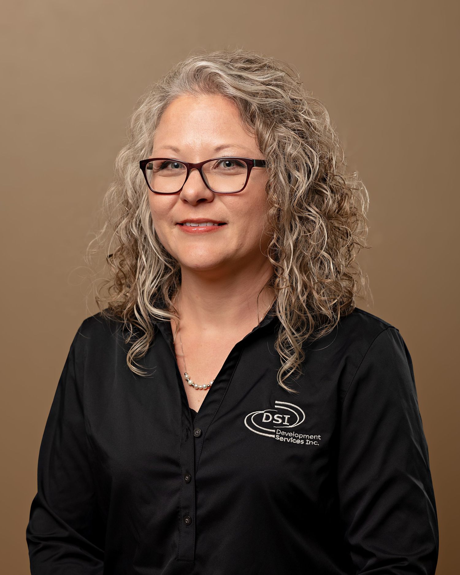 Professional headshot of curly gray-haired woman wearing black DSL company polo shirt.