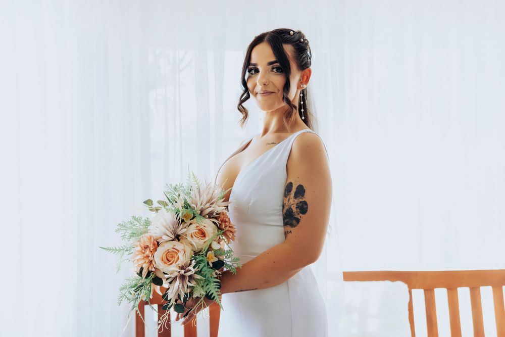 Bride in elegant white dress holding romantic peach and green floral bouquet.