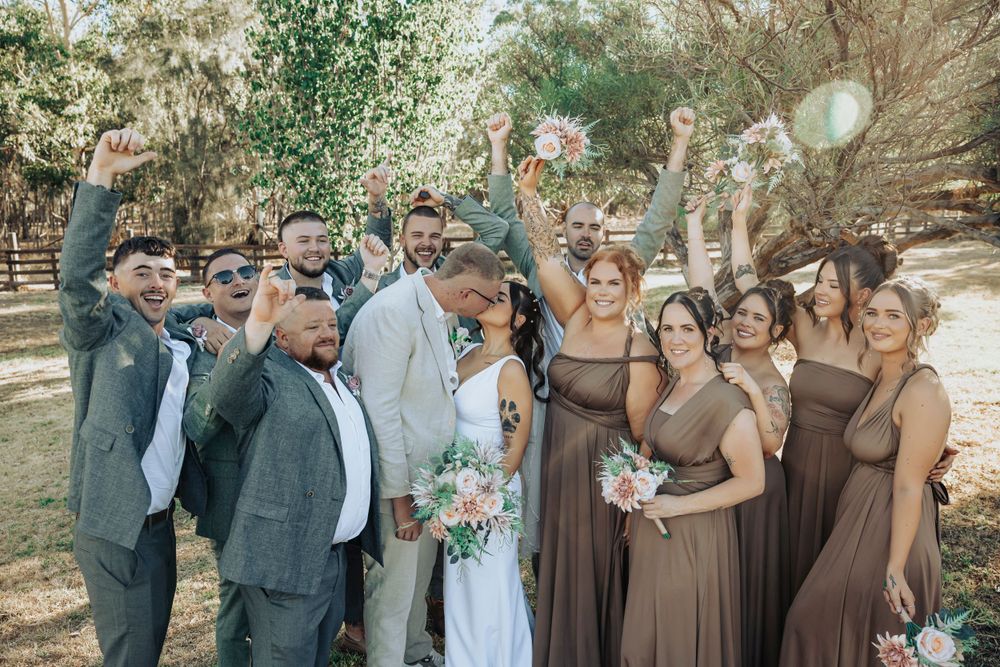 Wedding party celebrating outdoors with joyful expressions in brown and grey attire.