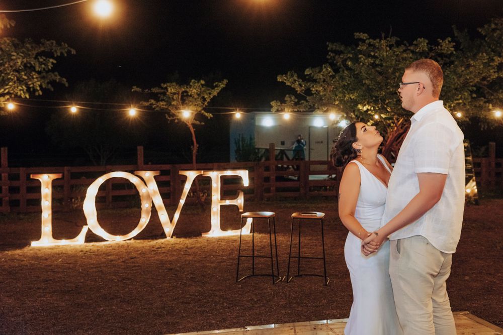 Couple standing in front of illuminated LOVE sign during evening reception.