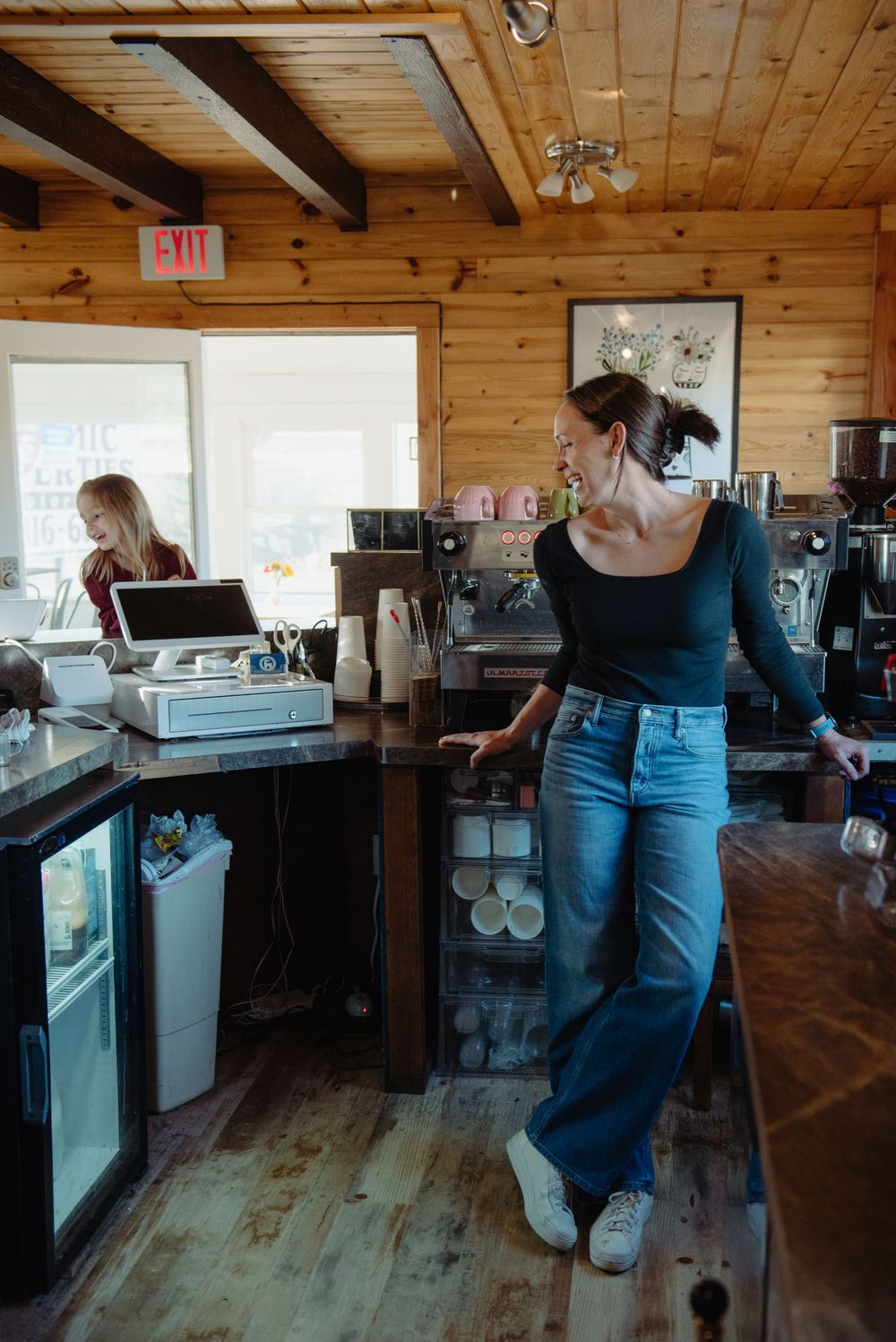 Coffee shop baristas working behind wooden counter with espresso machines and cafe equipment.