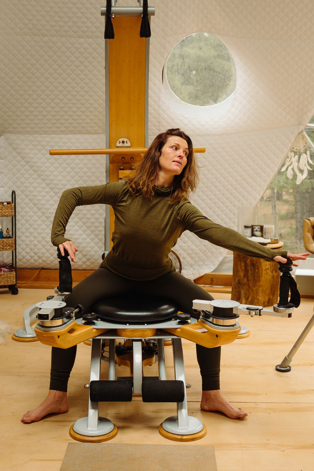 Woman stretching on unique wooden exercise equipment in bright studio space.