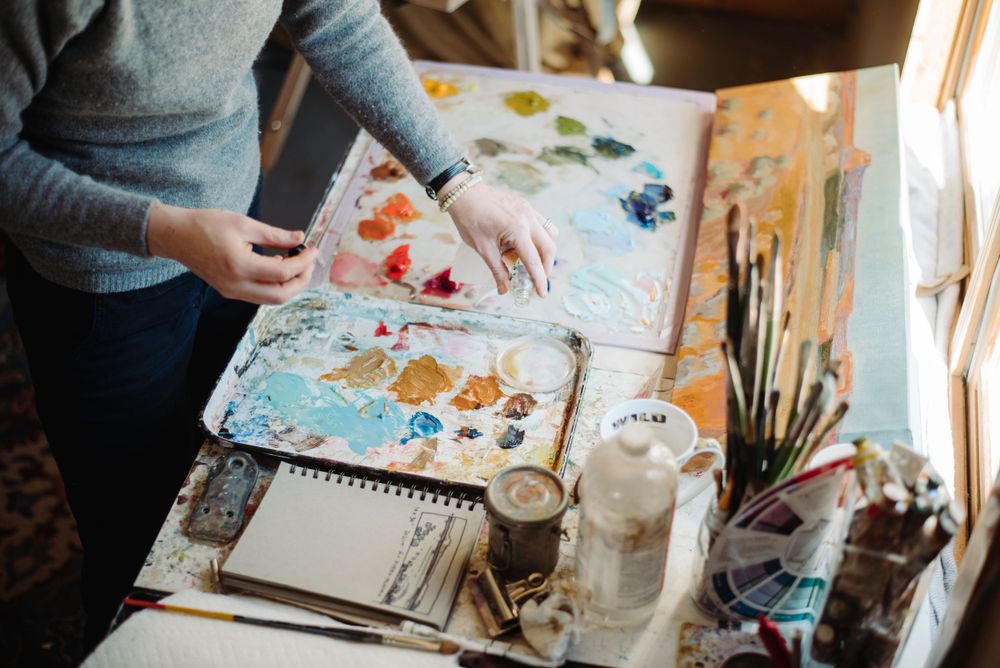 Artist working with colorful paints and art supplies on wooden table.