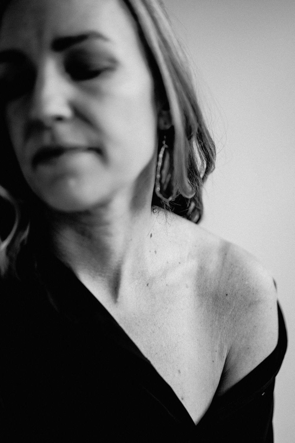 A black and white artistic portrait featuring a person in a dark top with bare shoulder against a plain background.