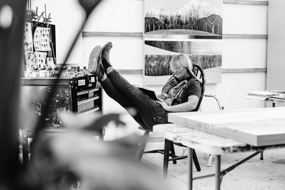 Black and white photo of artist relaxing in creative studio space with framed artwork.