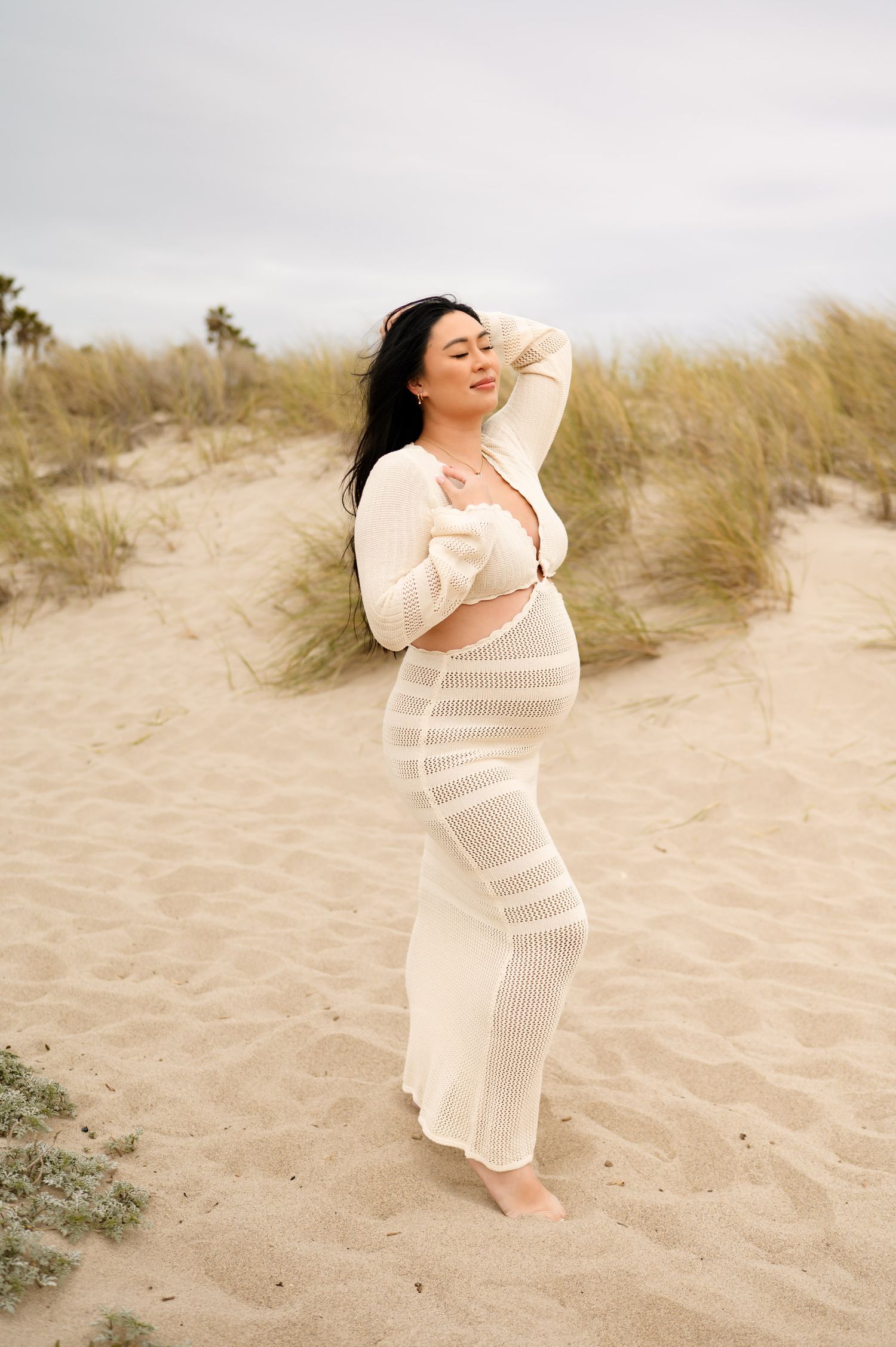 woman in JLuxelabel crochet dress poses in sand during her Carpinteria beach photoshoot by Santa Barbara maternity Photographer