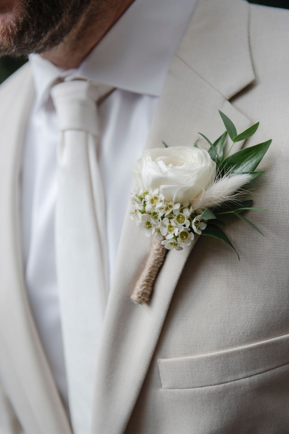 A classic white rose and baby's breath boutonniere adorns a cream-colored suit lapel.