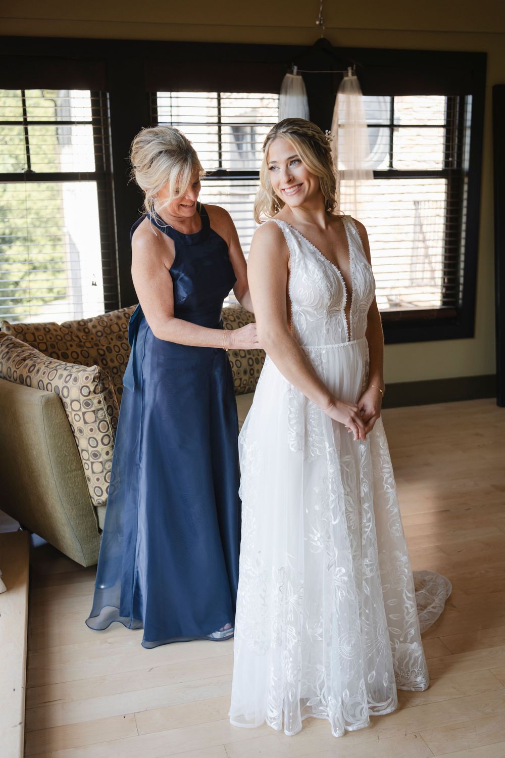 A special moment between mom and bride in formal dresses, one in navy blue helping adjust a white lace wedding gown.