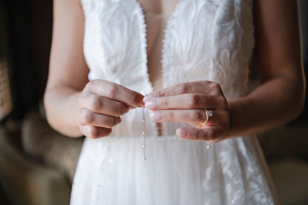 Close-up photo of hands holding a wedding earrings while wearing a white lace wedding dress.