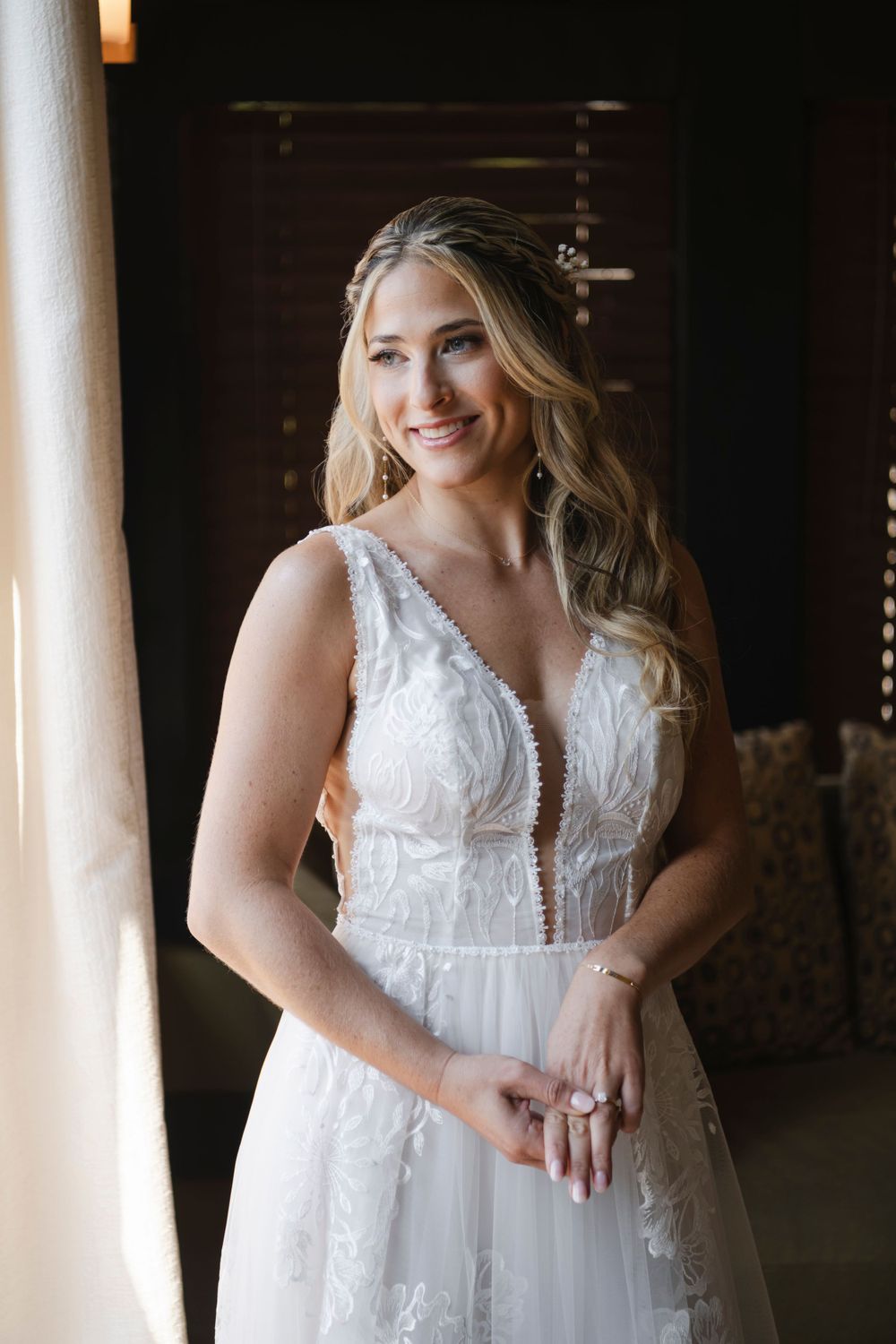 Beautiful bridal portrait showing ethereal white lace wedding gown with plunging neckline near a sunlit window.