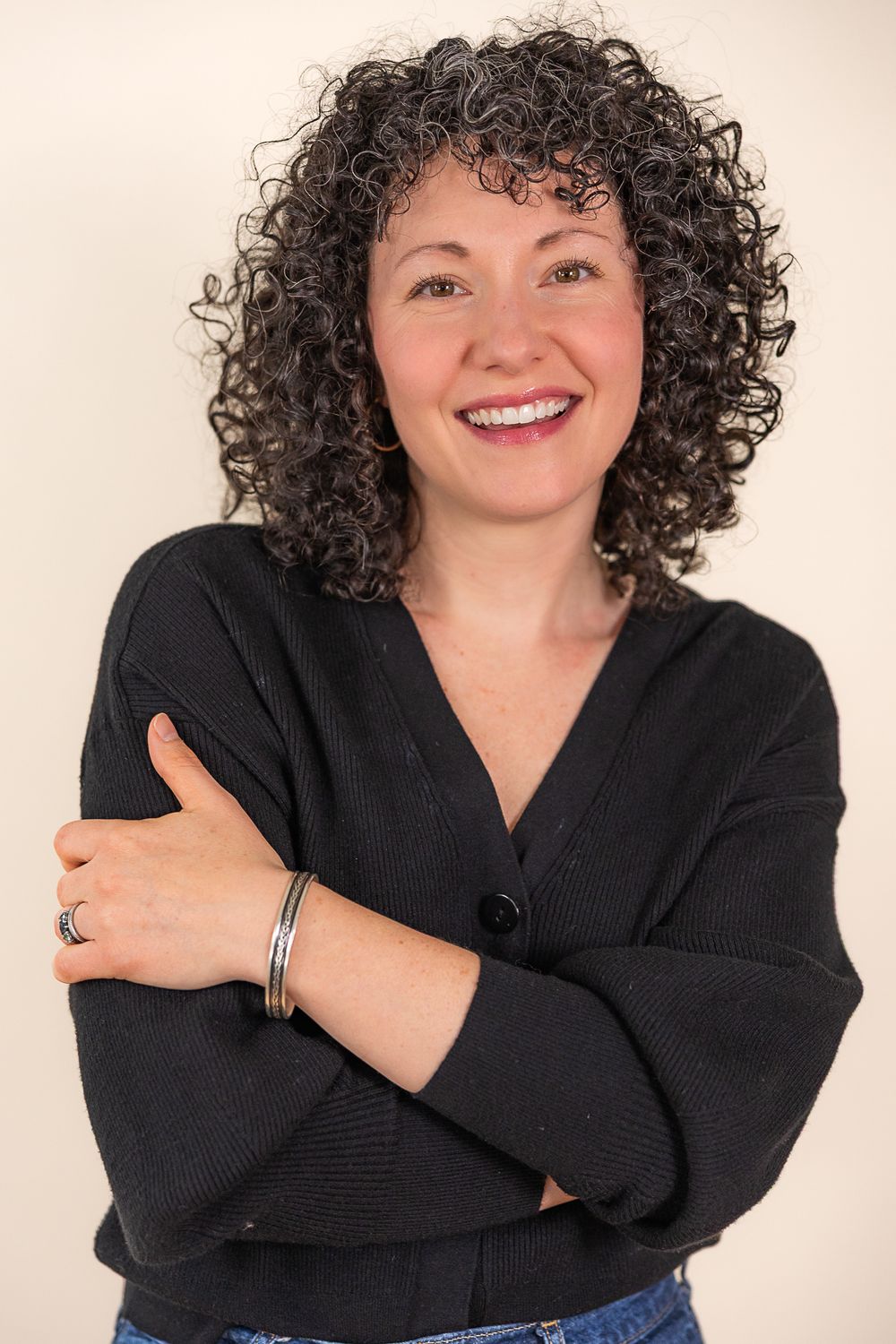 A person with curly dark hair wearing a black sweater poses playfully against a light background in four sequential photos.