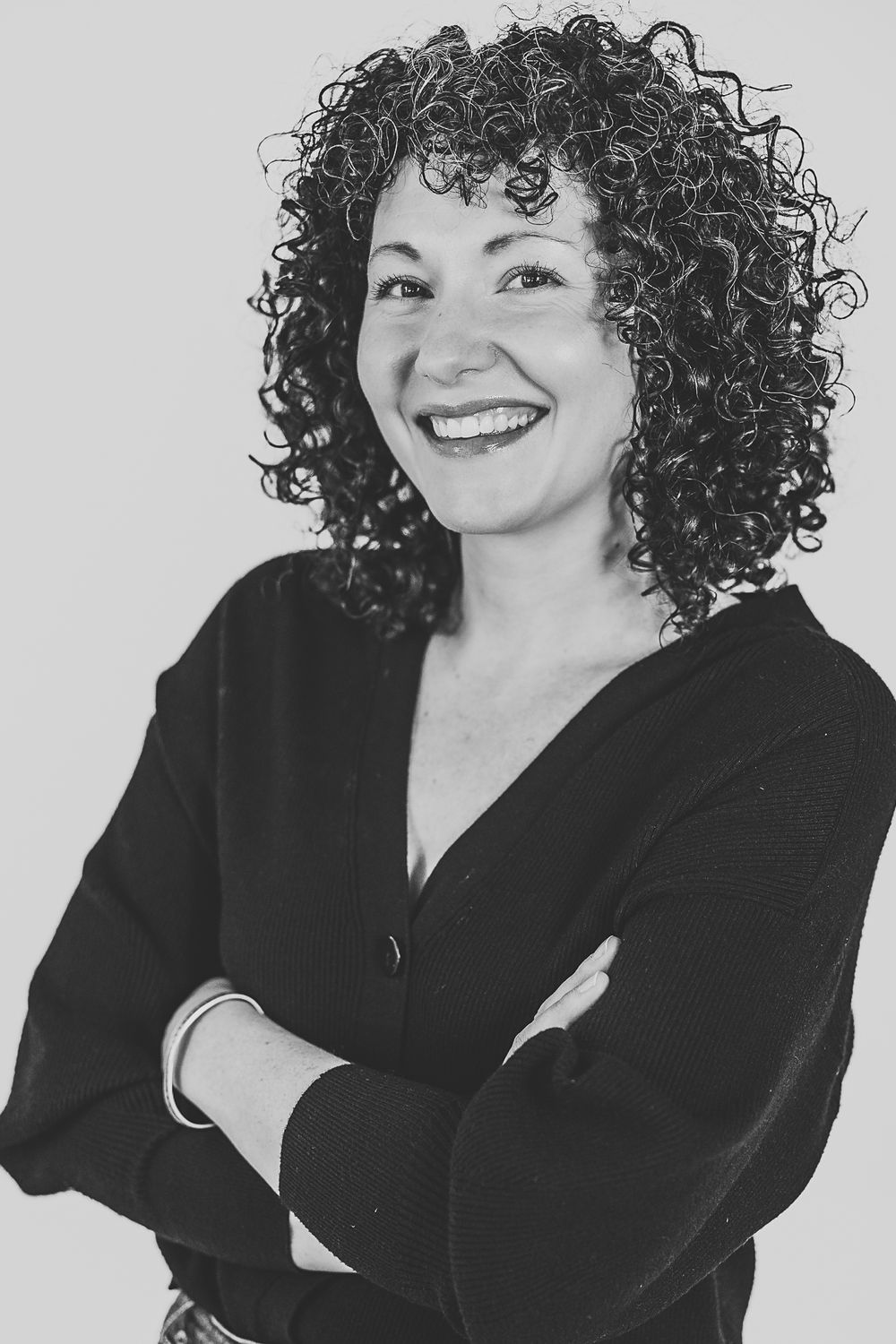 Black and white studio portraits show a person with curly dark hair and black blazer smiling in different poses.