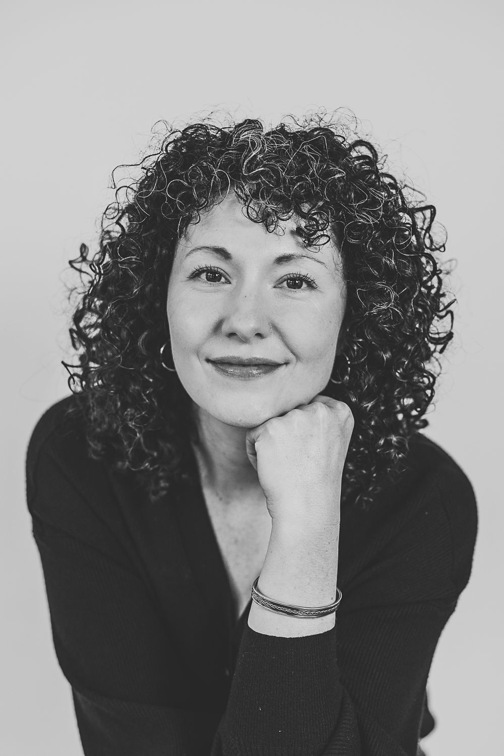 A black and white photo series showing someone with curly dark hair in various expressive poses against a light background.