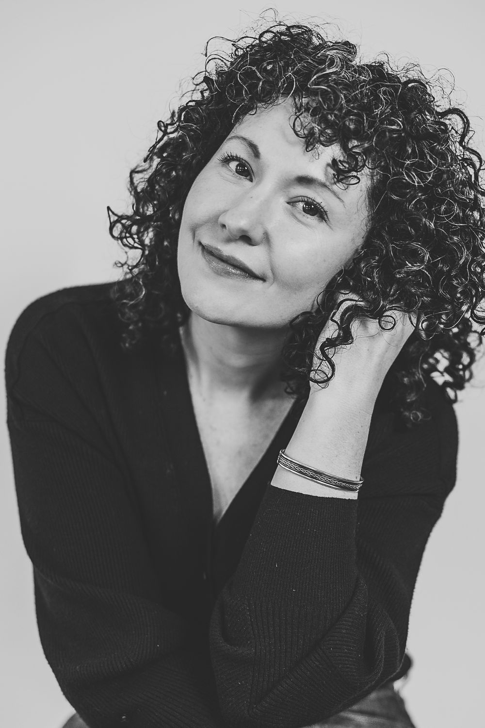 Black and white portrait series showing playful poses with curly hair against a light background.