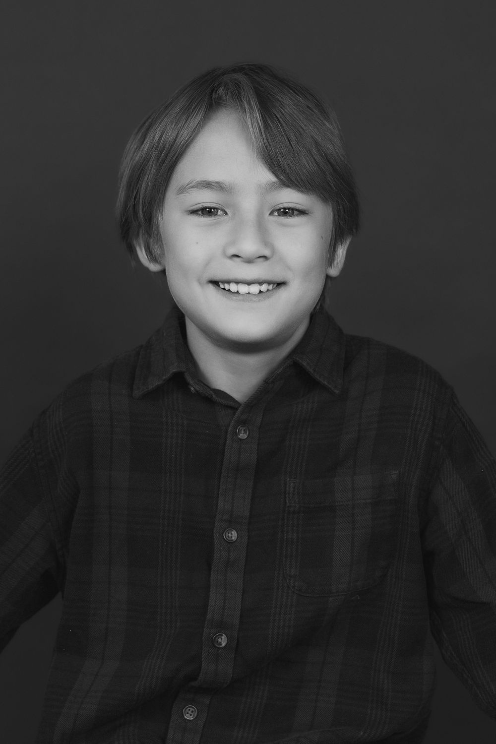 Black and white studio portrait of a young student smiling in a plaid shirt against a dark backdrop.
