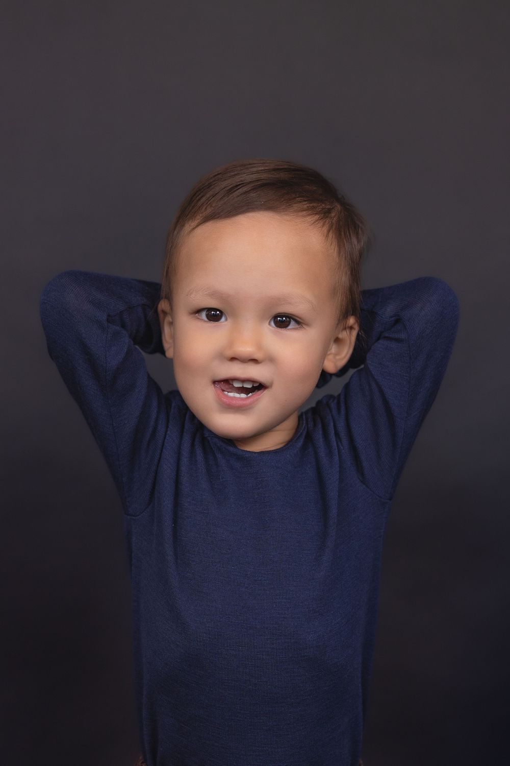 A smiling toddler in a navy blue sweater poses against a dark background in a series of connected photos.
