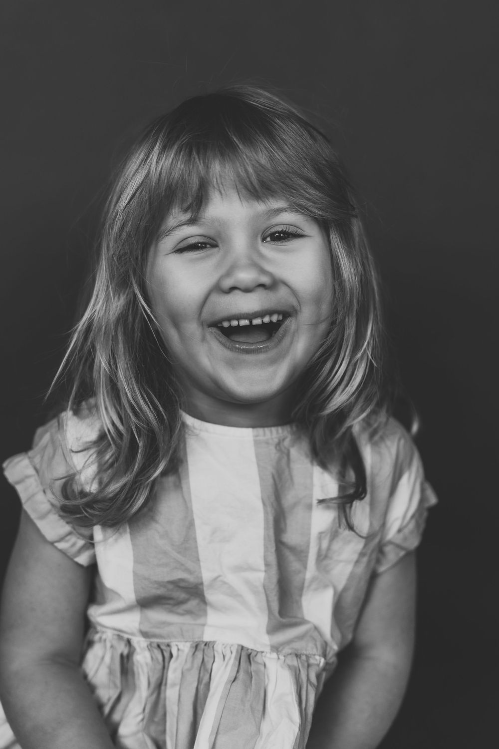 A series of black and white photos showing a child in a white dress expressing joyful emotions.