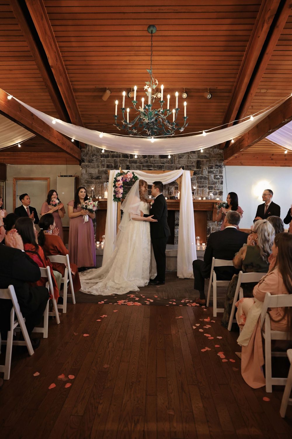 Bride and groom stand at the altar during an elegant indoor wedding ceremony with seated guests.