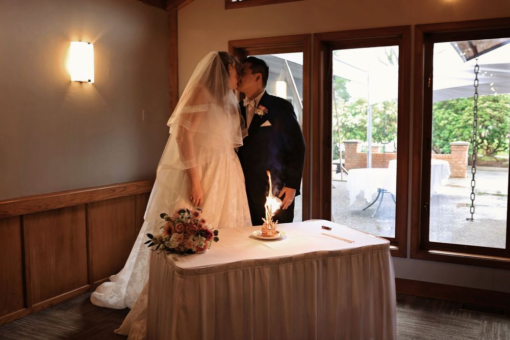 Bride and groom lighting a unity candle at wedding ceremony altar with floral arrangement indoors.