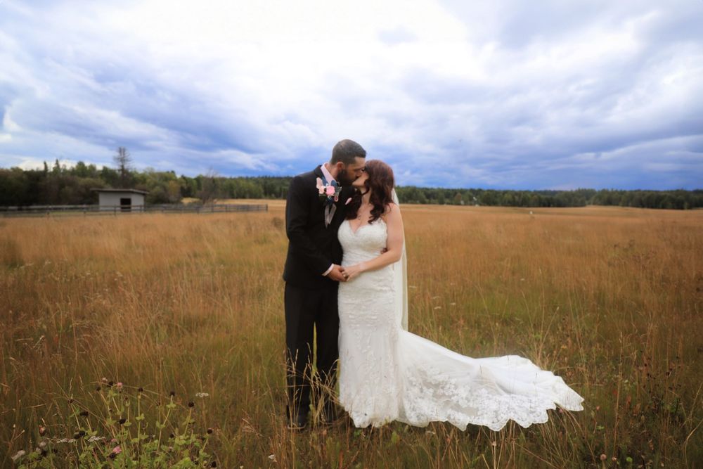 A tender moment between newlyweds in a rustic field with dramatic sky.