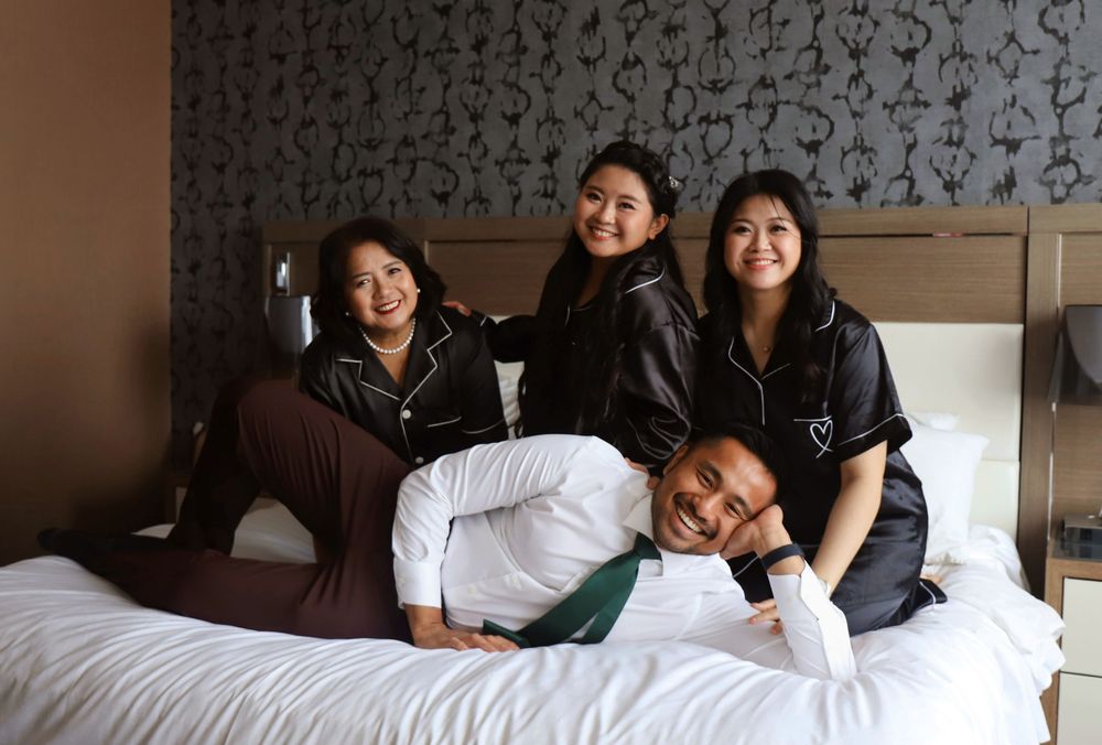 A group relaxes together on a hotel bed with patterned wallpaper in the background.