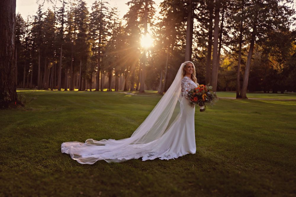 Wedding couple walking on grass lawn with tall pine trees at sunset.