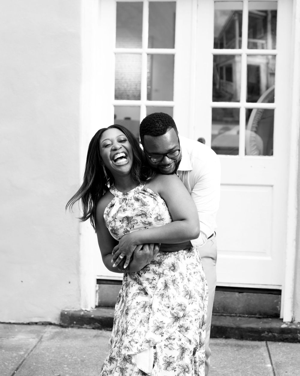 A couple laughs together during a romantic outdoor photo session in front of a white building.