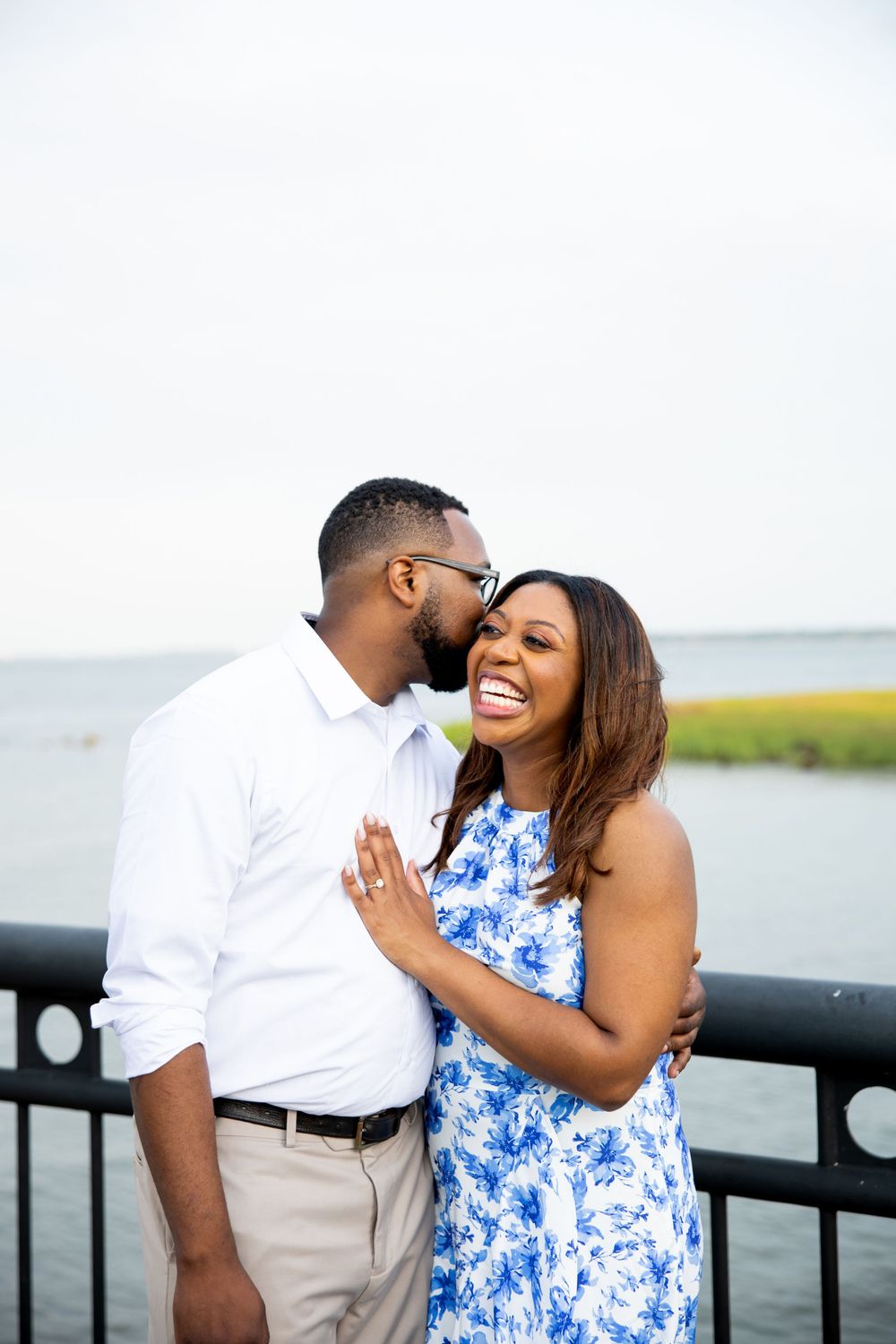 A joyful couple shares a tender moment while standing on a waterfront deck.