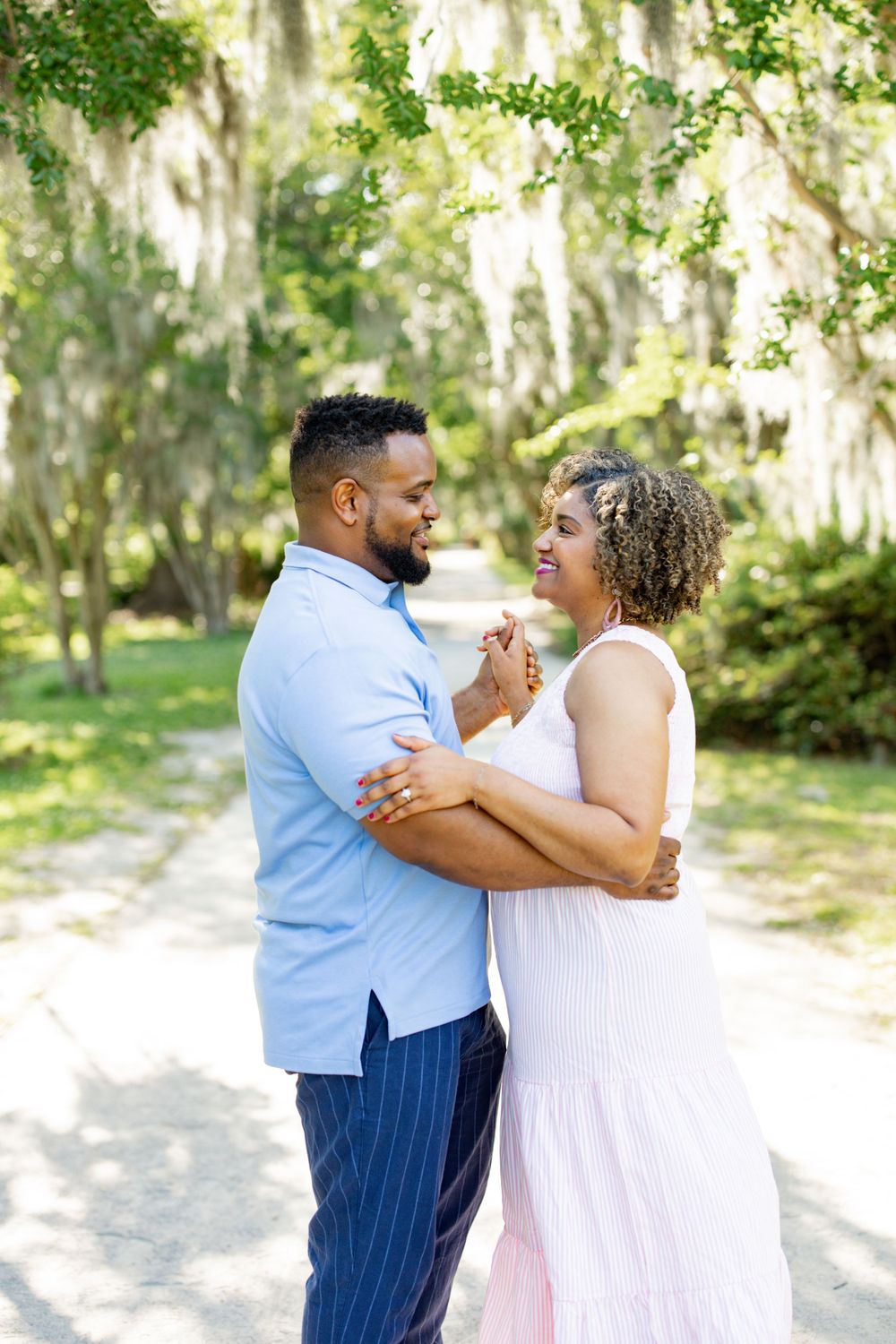 A romantic couple dancing together on a sunlit path surrounded by Spanish moss and greenery.
