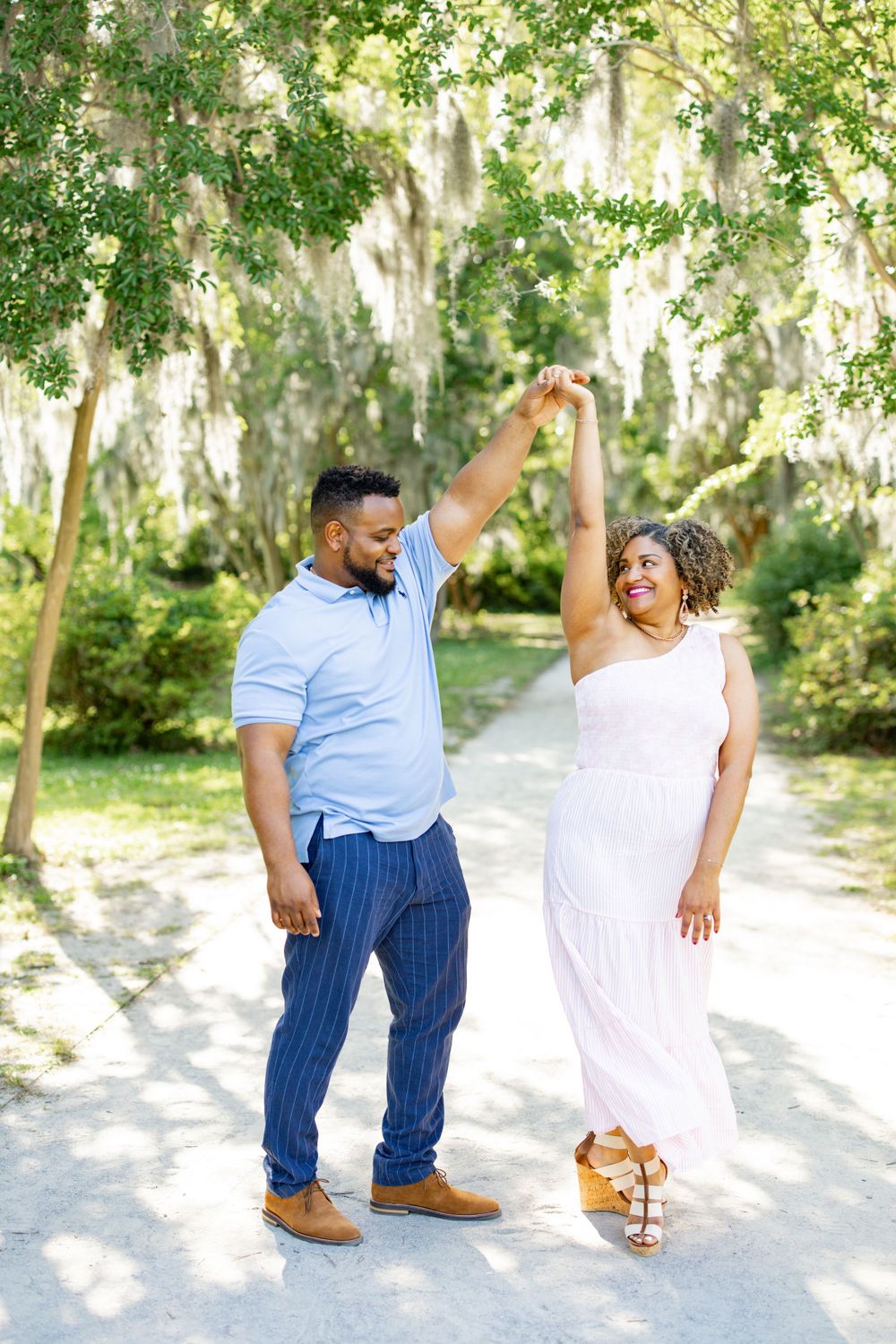 A couple dances together while holding hands on a pathway with hanging moss overhead.