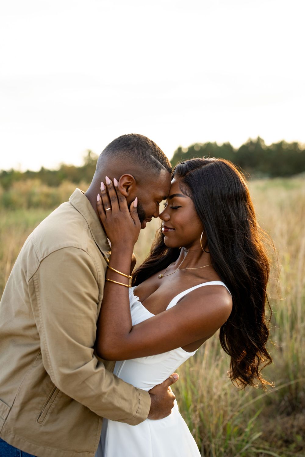 Romantic outdoor portrait of a couple embracing tenderly in a golden field at sunset.