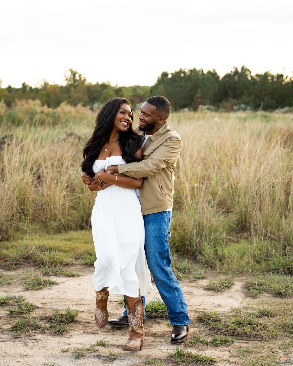A couple embraces and laughs together in a sun-lit field of tall grass during a joyful outdoor photoshoot.