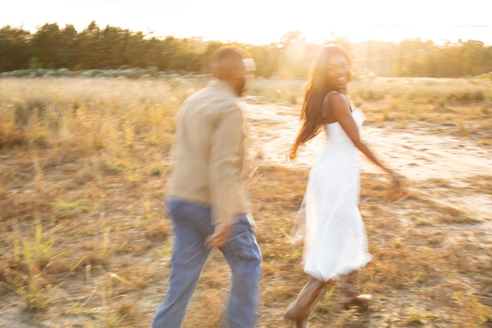 A couple walks hand in hand through a sunlit field at golden hour creating a dreamy motion blur effect.