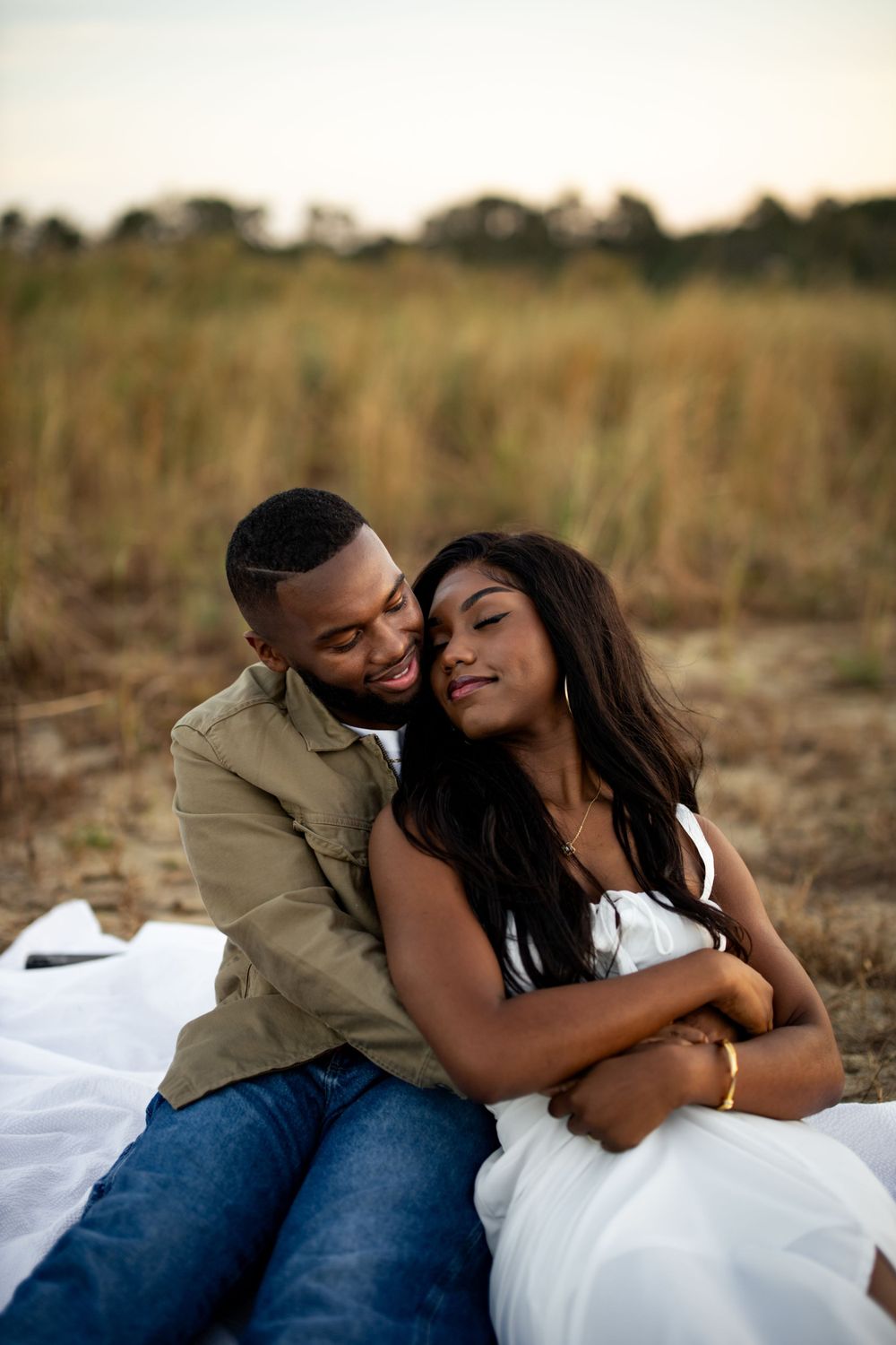 A romantic couple shares an intimate moment while relaxing together on a blanket in a field at sunset.