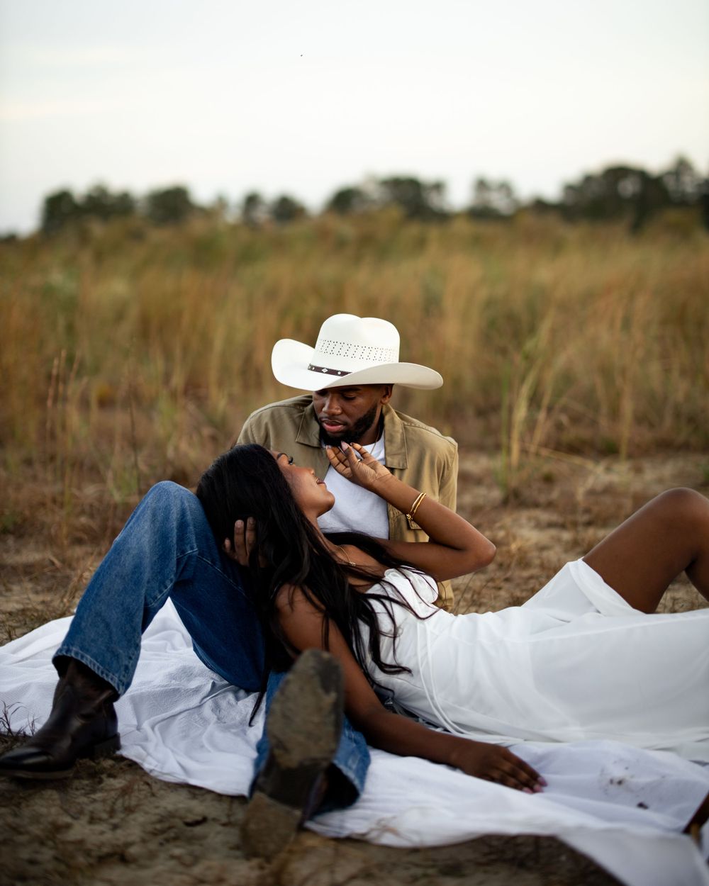 A couple laughs and embraces while laying in a rustic field during a romantic photoshoot.