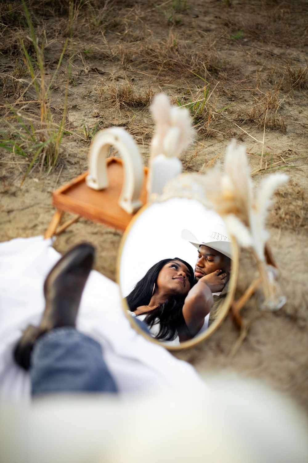 A decorative mirror lying on dry grass ground reflects white and brown natural tones.