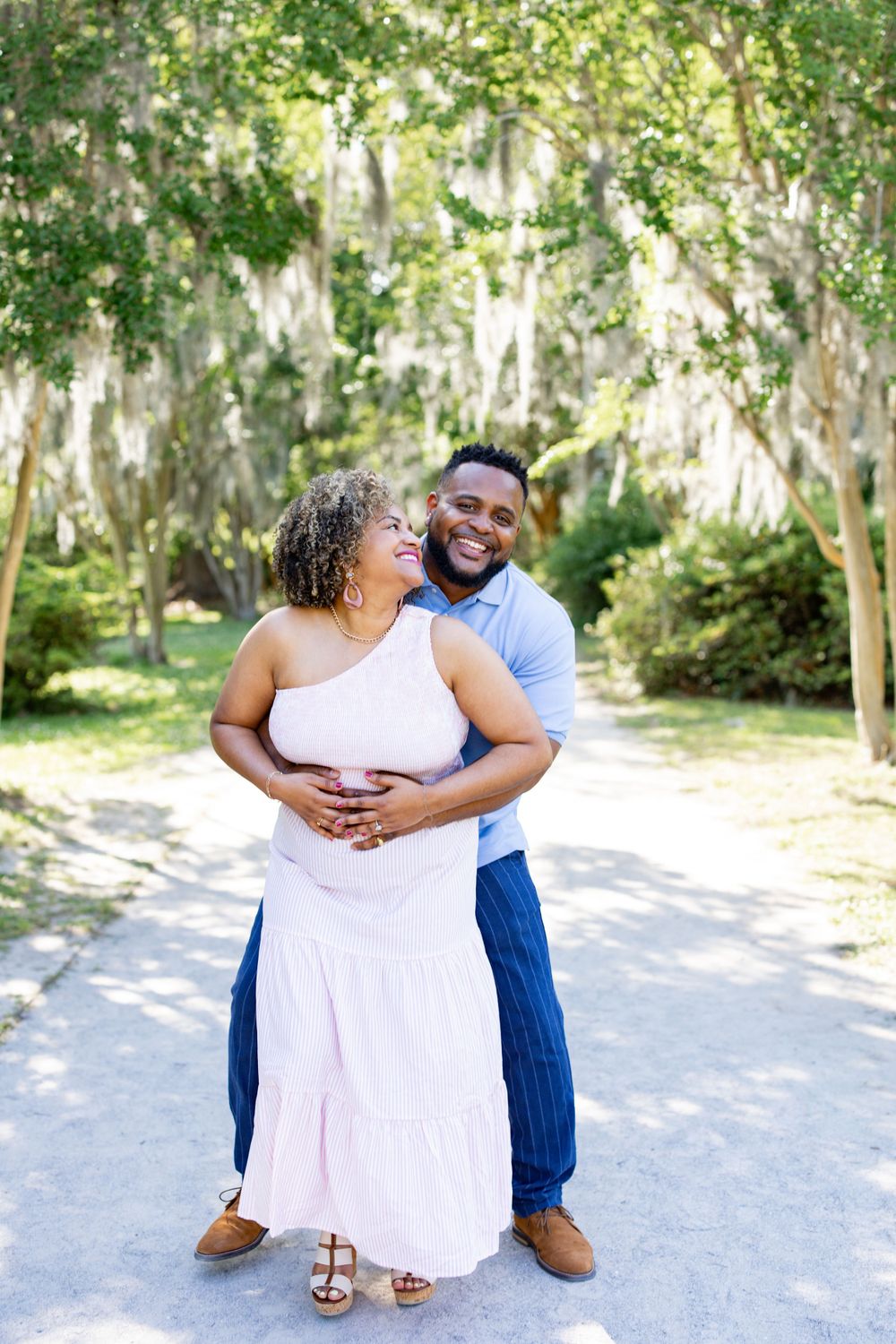 A couple embraces while sharing a romantic moment on a tree-lined path.