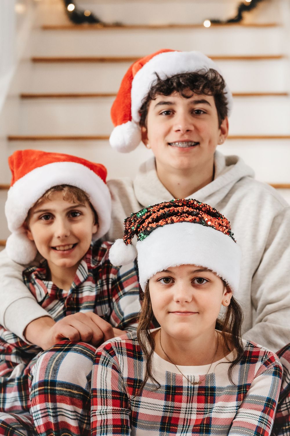 Children wearing Santa hats and plaid shirts pose for holiday portrait.