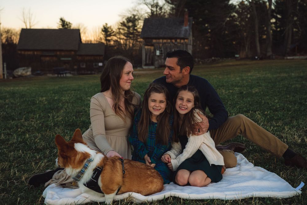 Family and dog relaxing on blanket during sunset photoshoot.