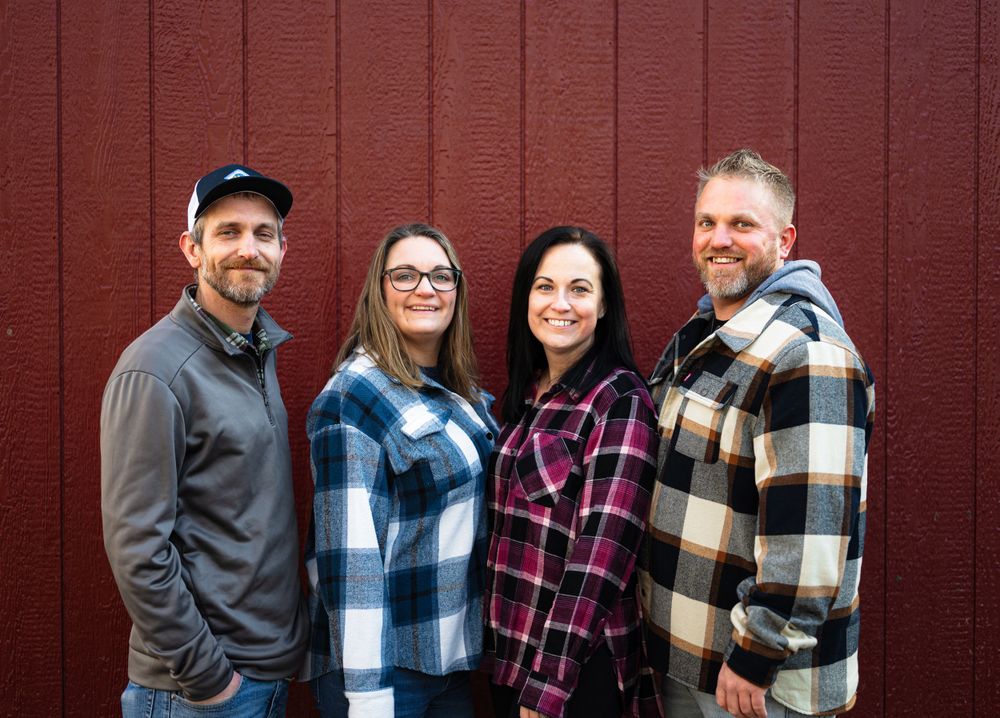 Group portrait of family members against red barn wall wearing casual attire.