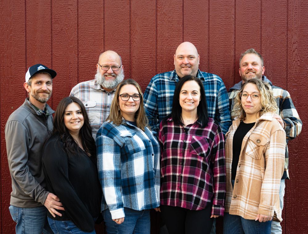 Extended family gathering wearing plaid shirts posed against red barn exterior.