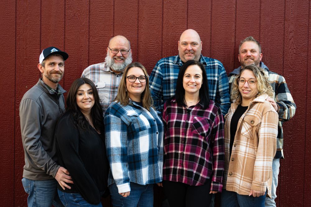 Large family group photo with multiple generations against red barn siding.