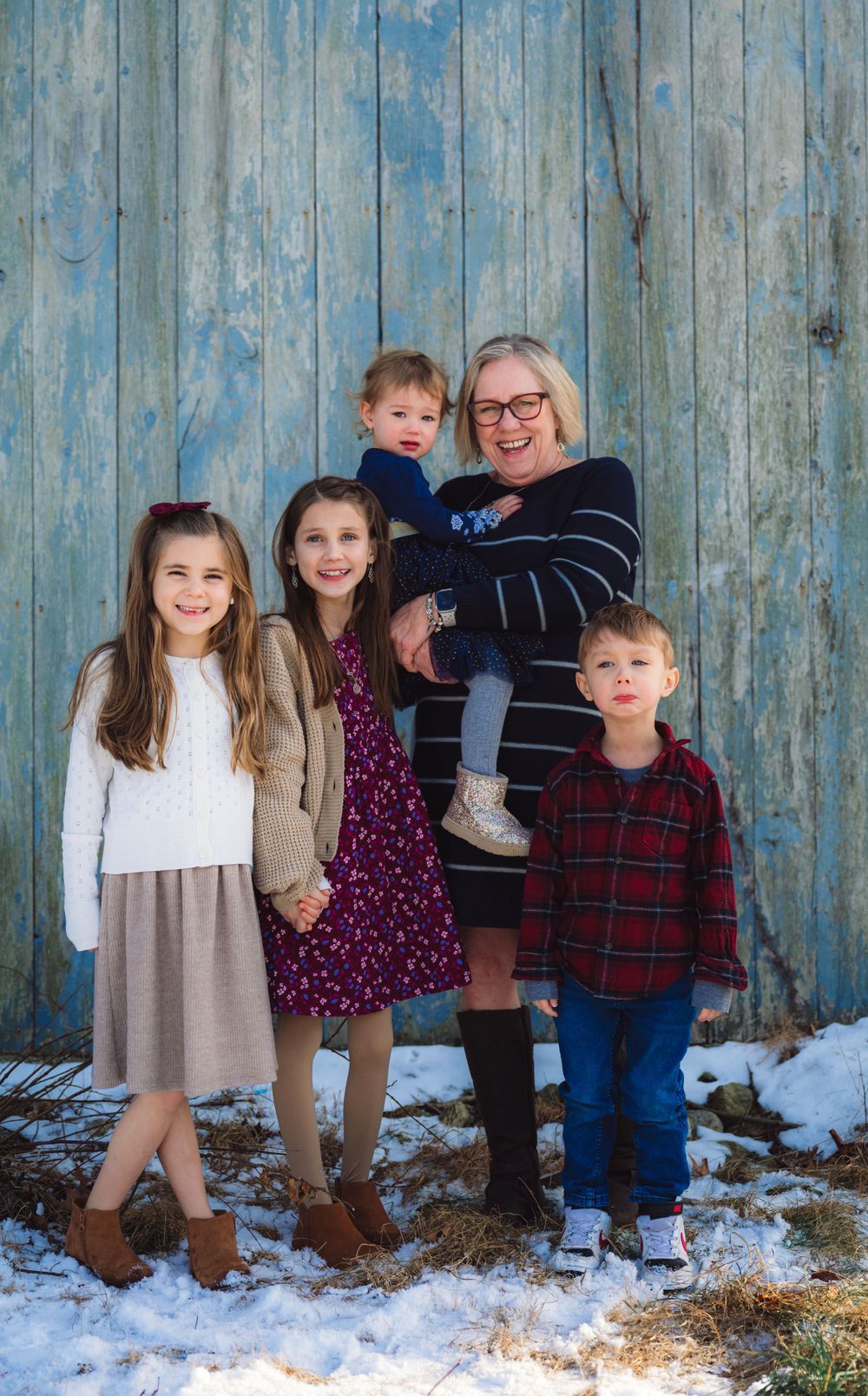Family group portrait against blue wooden wall with snow on the ground.
