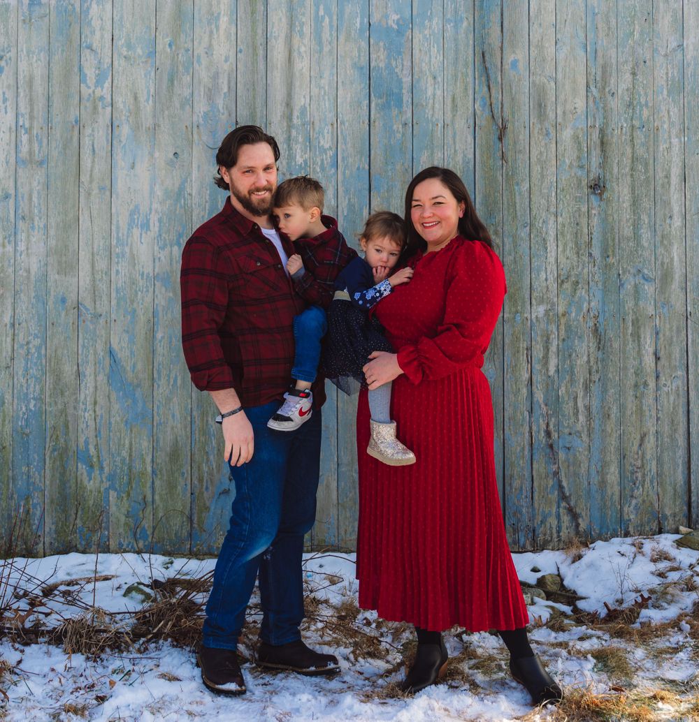Casual family portrait against weathered blue wall in winter setting.